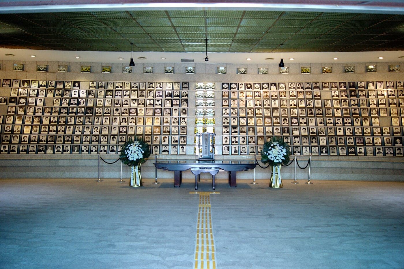 A long wall of framed portraits above an altar flanked by white wreaths.